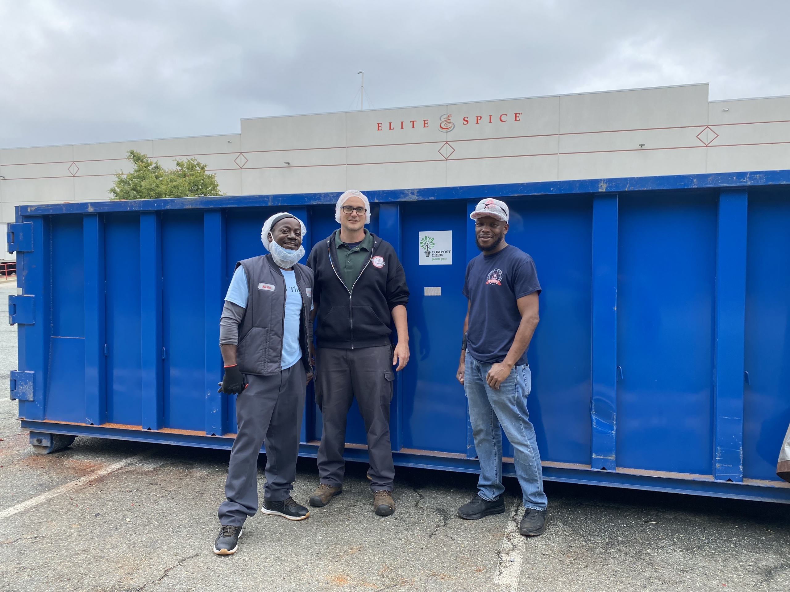 team members in front of the compost dumpster at Elite Spice